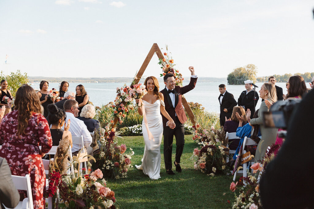 A couple walks down the aisle at their fall wedding at The Lake House on Canandaigua, after a lakeside ceremony in the Finger Lakes of NY.