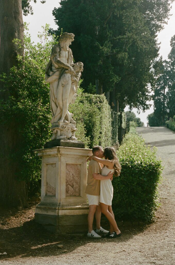 An engagement session at Baboli Gardens in Florence, Italy. A couple kisses in front of a garden sculpture.