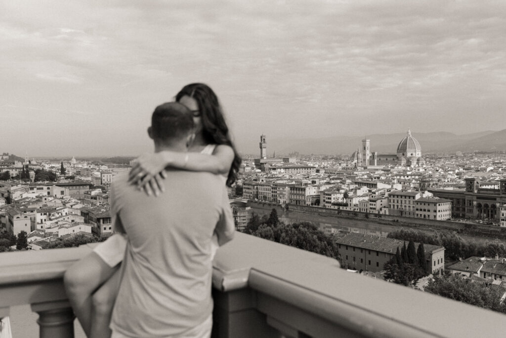 A couple kisses during their engagement session, overlooking the city of Florence Italy from Piazzale Michelangelo.