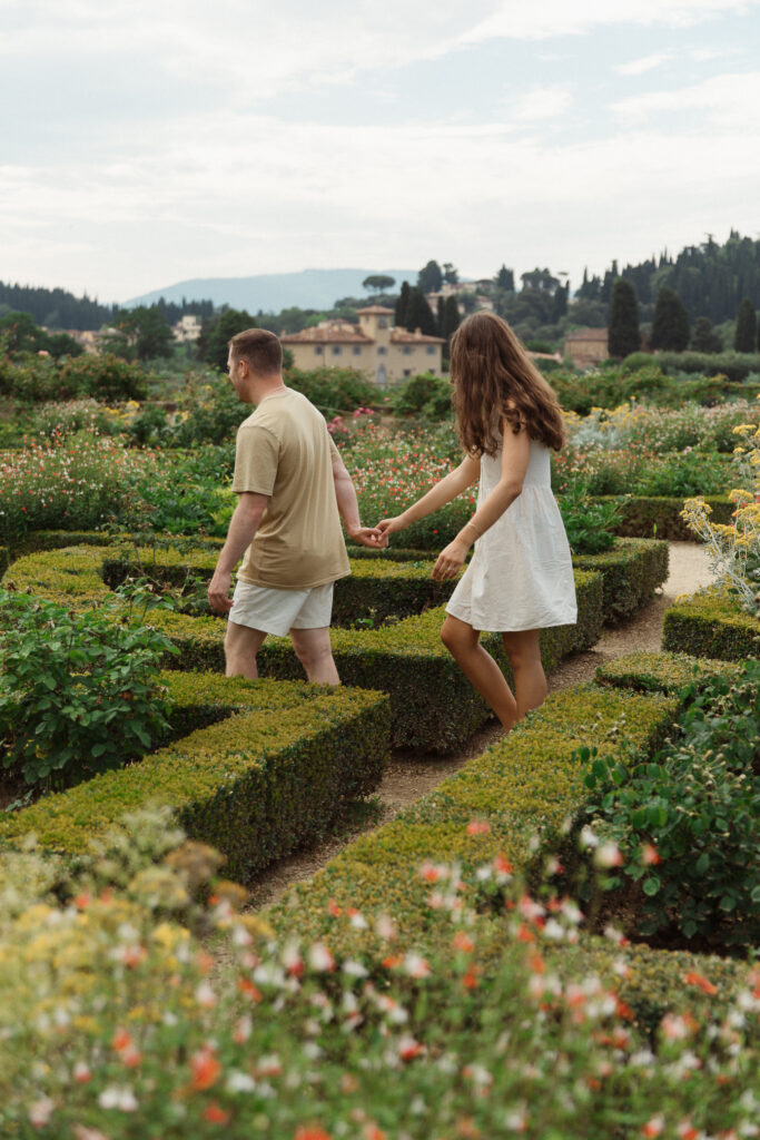 In the Gardens of Baboli in Florence, Italy, a couple holds hands and walks through the flowers for their engagement session.