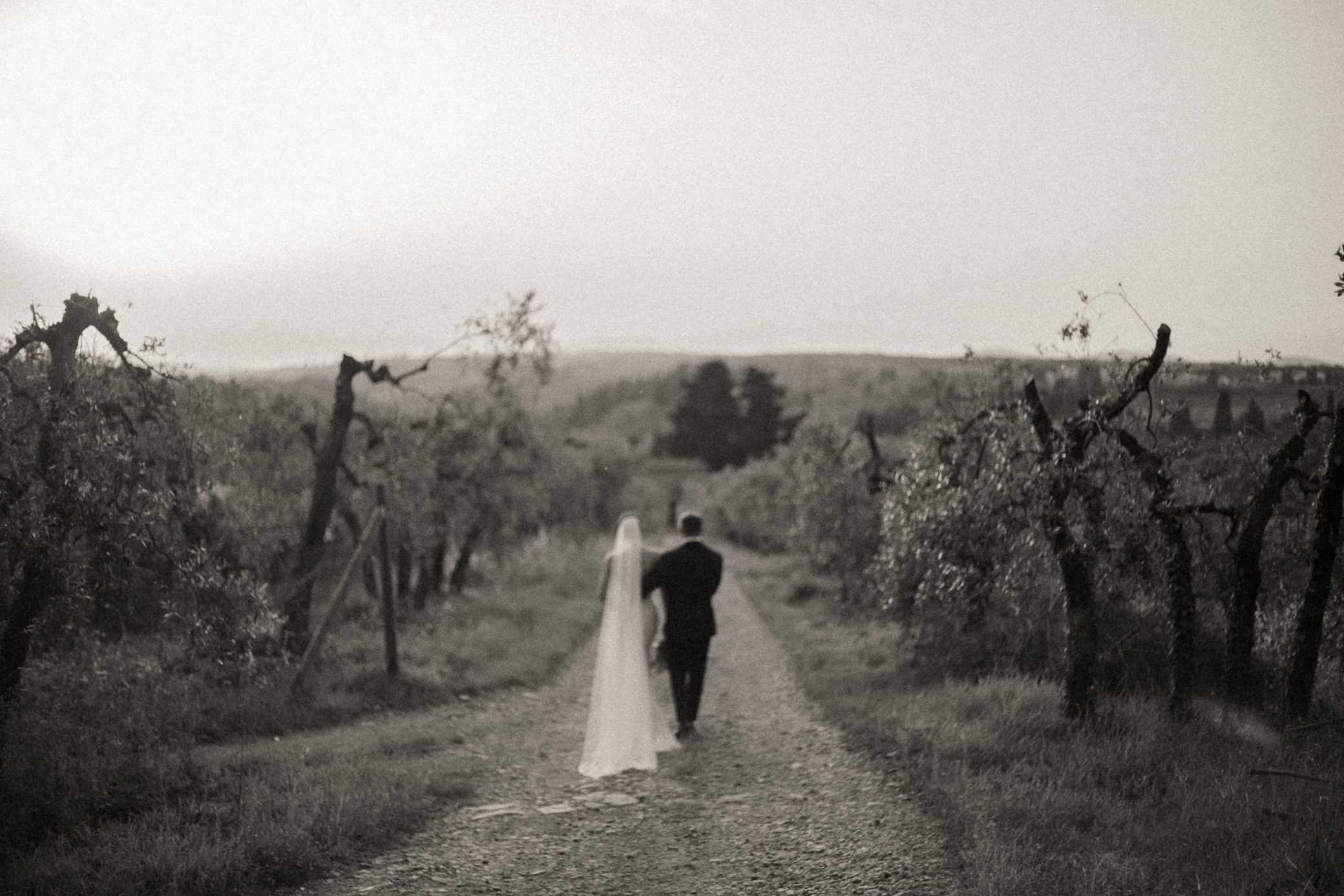 A couple walks through a vineyard at their destination wedding in Italy. Taken at Castello il Palagio by By Bridget Photography.