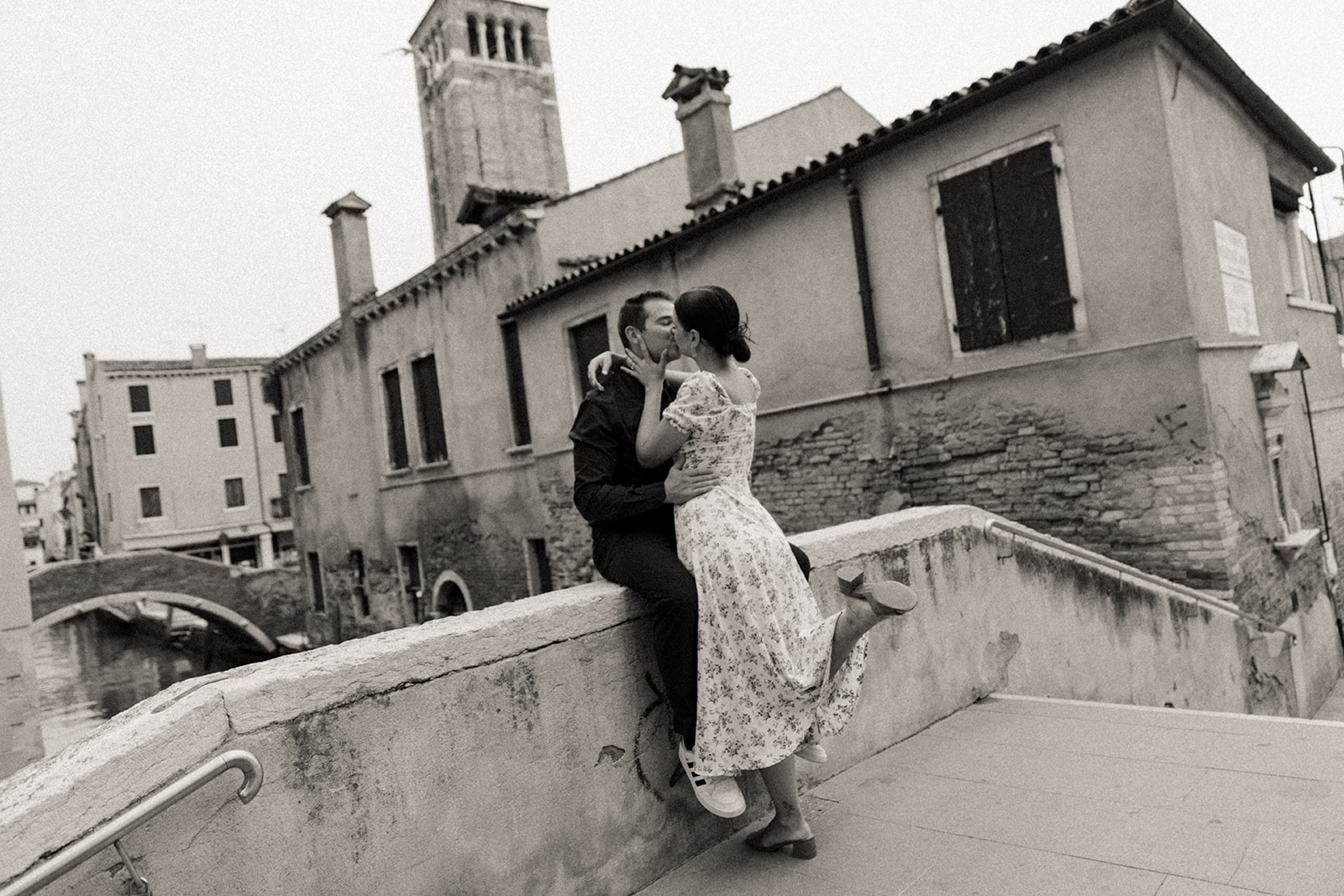 A couple kisses on a bridge over a canal during their destination engagement session in Venice, Italy. By Bridget Photography