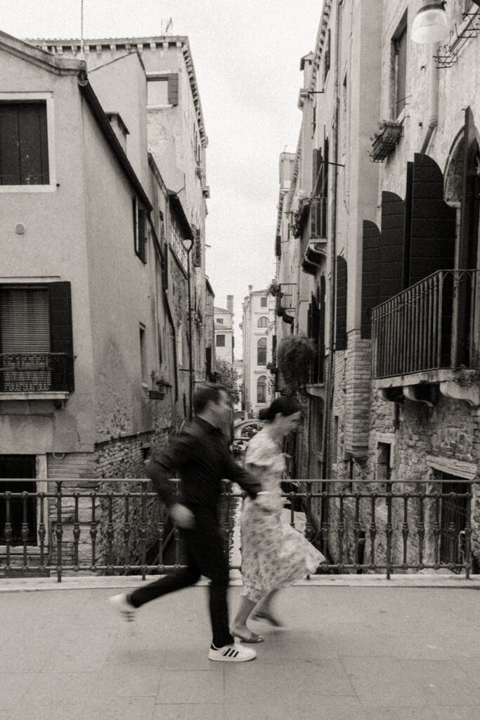 A couple runs over a canal bridge together in Venice, Italy for their engagement session.